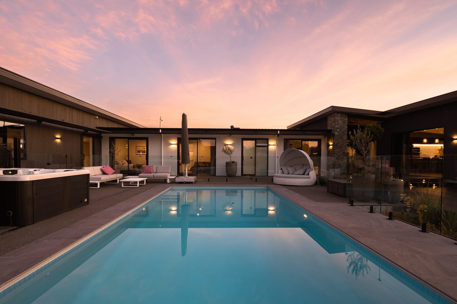 A Discovery Homes new build at dusk with pool, hot tub, and warm interior lighting